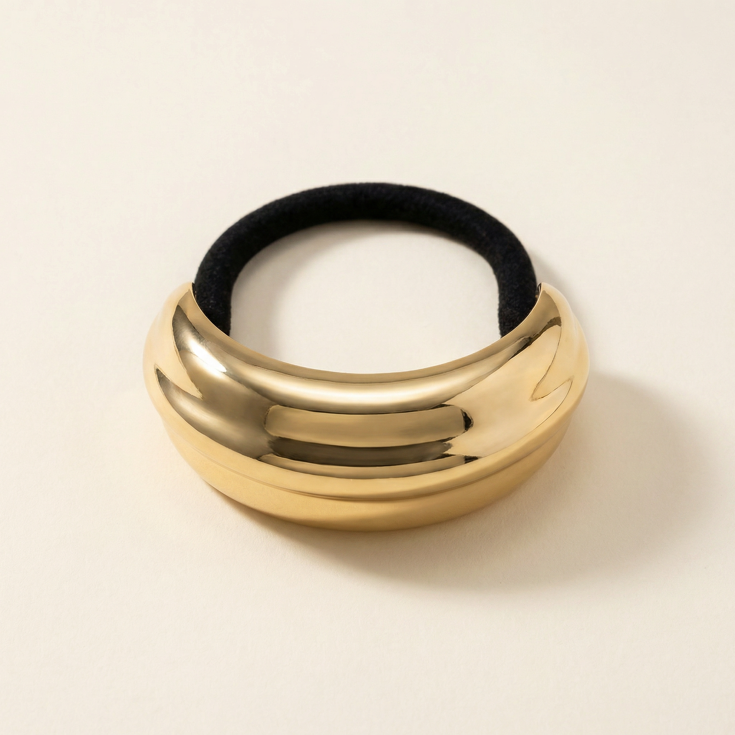 Gold metal pony cuff with black rubber band on a beige background - Snug Strands